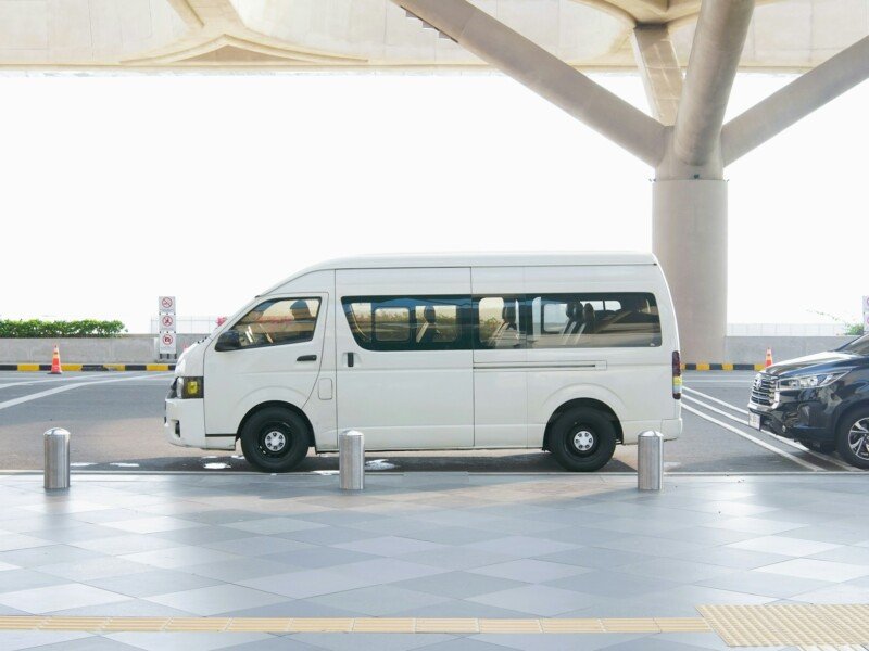 White transfer van waiting at an airport terminal drop-off zone